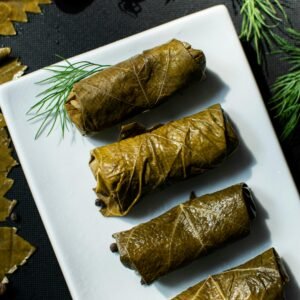 Appetizing dolma wrapped in grape leaves served with dill and cherry tomatoes.
