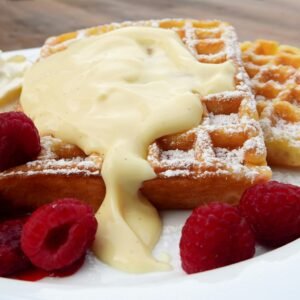 Close-up of waffles topped with cream and raspberries, perfect for breakfast.