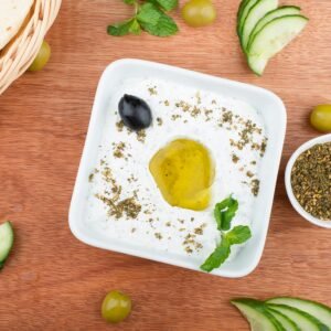 Close-up of labneh topped with olive oil and herbs, garnished with mint and olives.