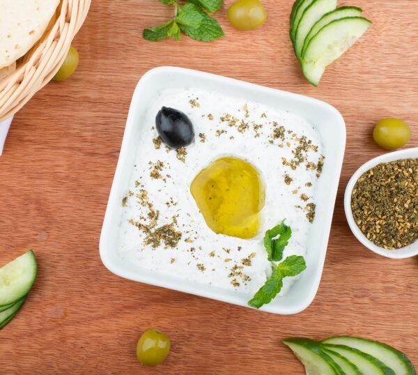 Close-up of labneh topped with olive oil and herbs, garnished with mint and olives.